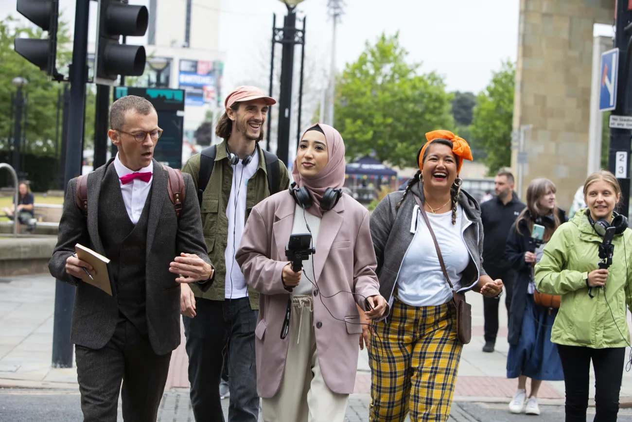 Four adults walking through Bradford with headphones and eccentric dress, taking part in Story Trails
