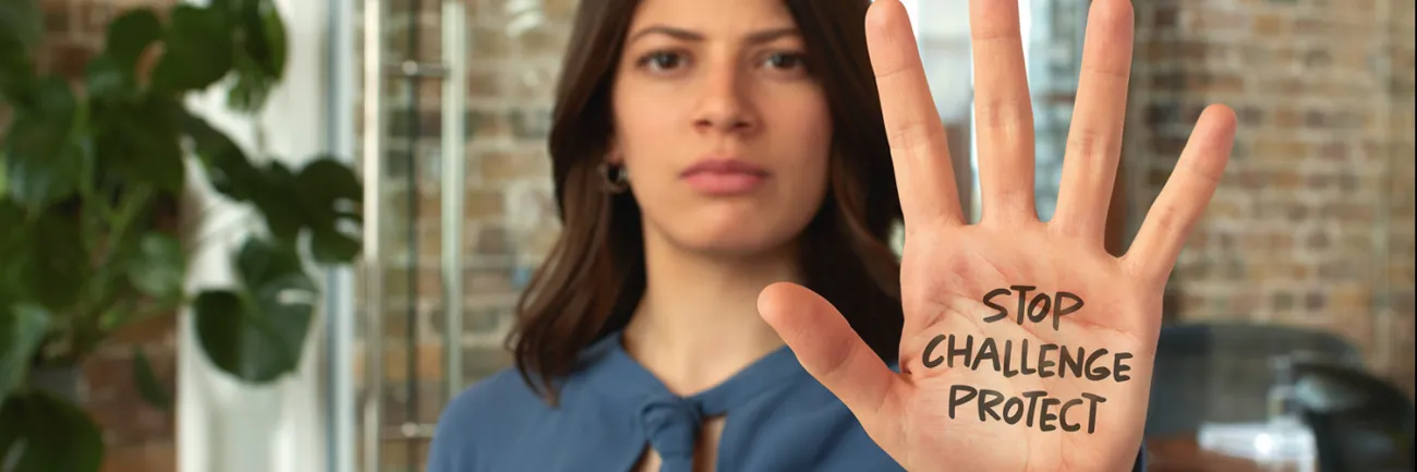 A woman holding up her hand and looking stern with the words 'stop, challenge, protect' written on her palm